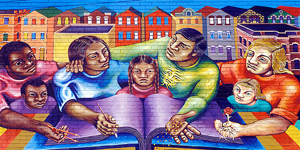 A brightly colored mural of illustrated adults and children sitting at a table with a large book. The group sits in front of a backdrop of multicolored homes.